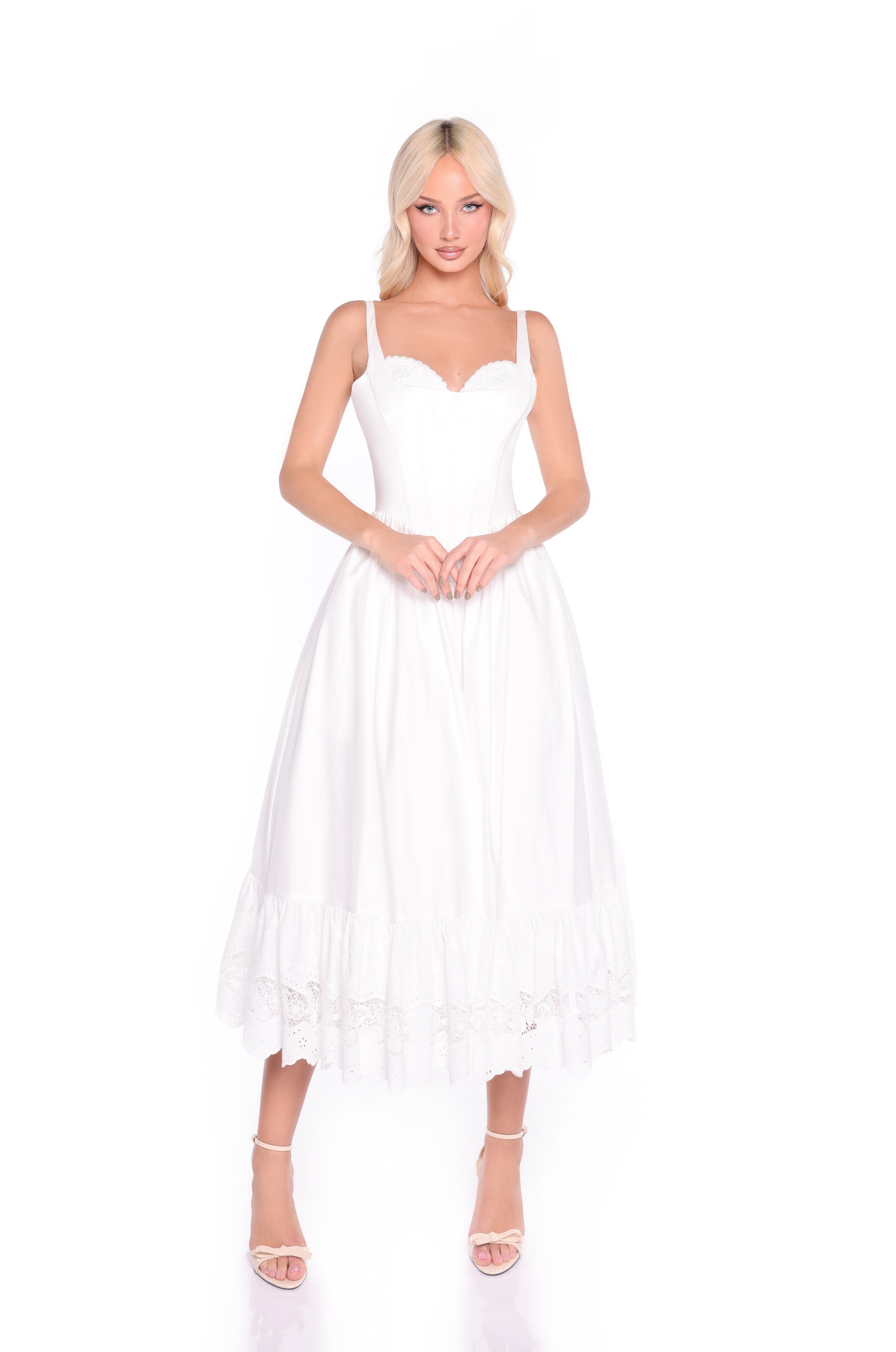 A woman stands against a white background wearing the White Casual Midi Dress: Celeste—sleeveless, white, midi-length with lace trim at the hem and a subtle corset bodice detail.